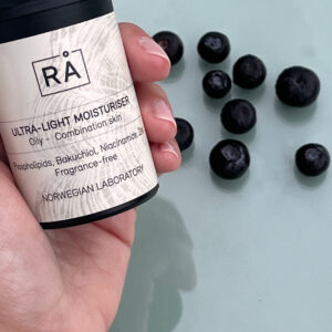 Ultra-Light Moisturiser holdt i hånden med blåbær på turkis bakgrunn