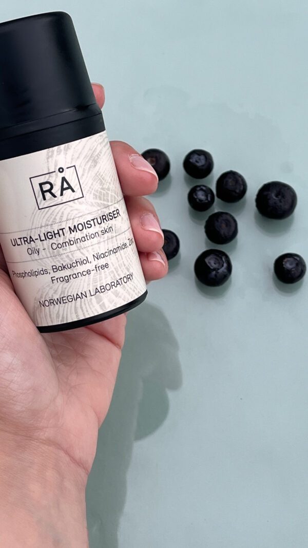 Ultra-Light Moisturiser holdt i hånden med blåbær på turkis bakgrunn
