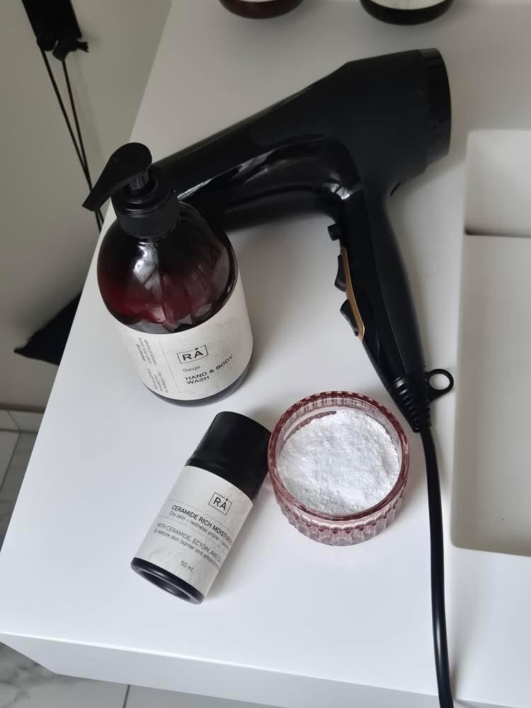 Ceramide fuktighetskrem fra RÅ Skincare for sensitiv hud på badet sammen med hårføner og toalettartikler.