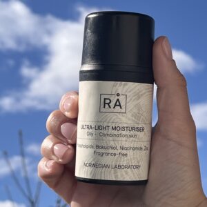 Produktbilde av lett, parfymefri fuktighetskrem holdt opp mot himmelen med skyer i bakgrunnen.