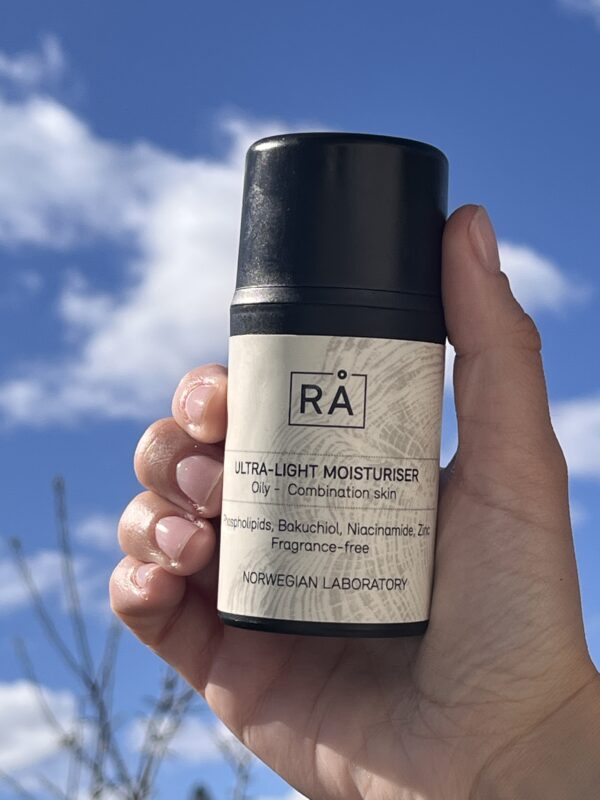 Produktbilde av lett, parfymefri fuktighetskrem holdt opp mot himmelen med skyer i bakgrunnen.