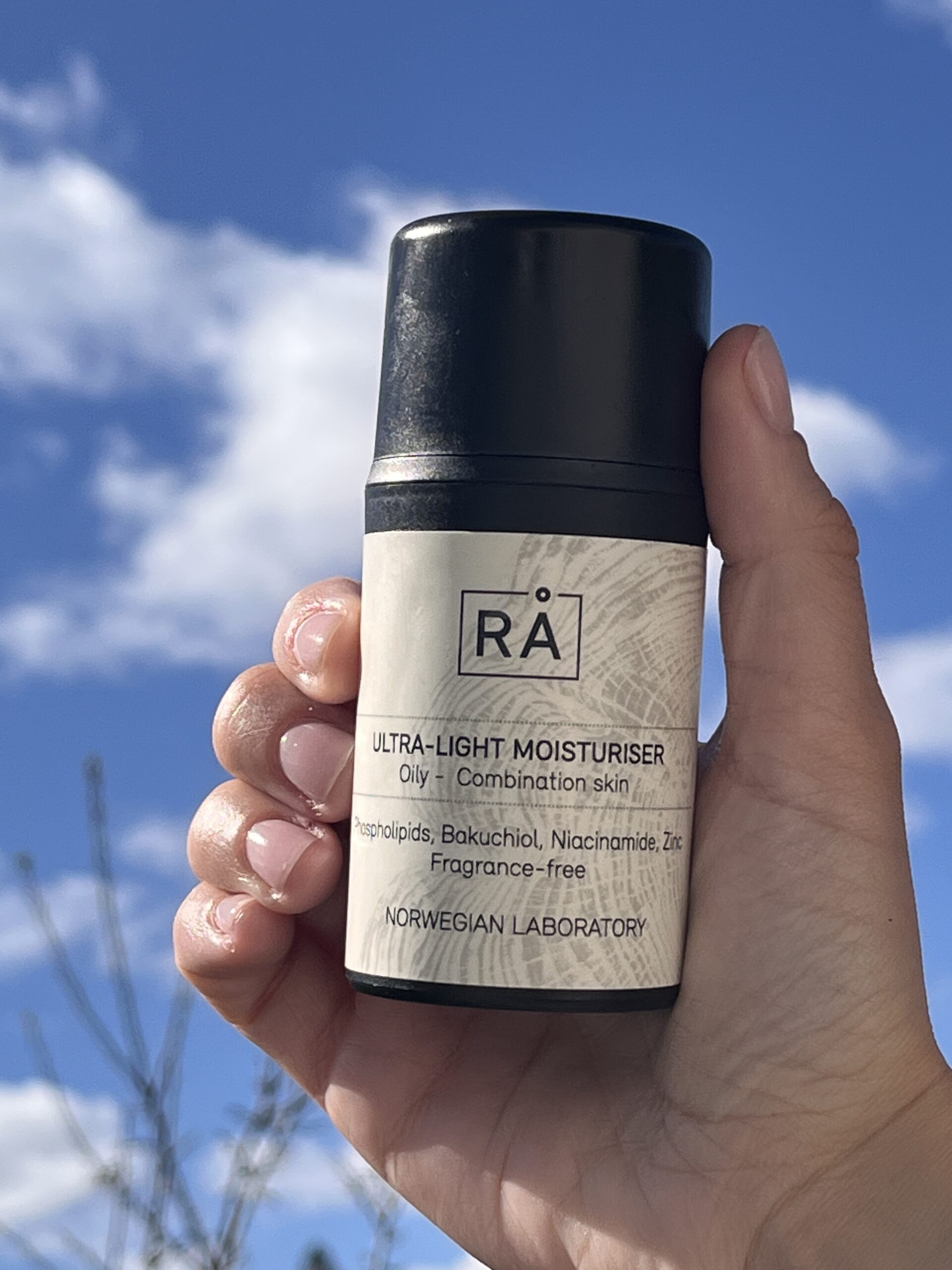 Produktbilde av lett, parfymefri fuktighetskrem holdt opp mot himmelen med skyer i bakgrunnen.