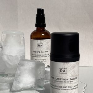 Pure Lipid Cleanser og Pore Clarifying Cleanser fra RÅ Skincare, presentert sammen som dobbelrens på lys bakgrunn med isbiter for en frisk følelse.